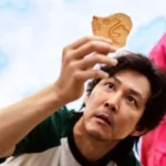 Close-up scene of a man carefully holding a honeycomb candy during a Korean survival game challenge