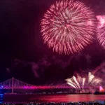 Colorful fireworks exploding over a lit bridge at night during a waterfront festival