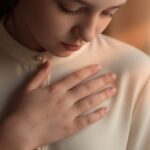 Close-up of a person's hand pressed gently to their chest with eyes closed in a moment of deep feeling