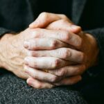 Close-up of tightly clasped hands in a lap showing tension and quiet anxious dread