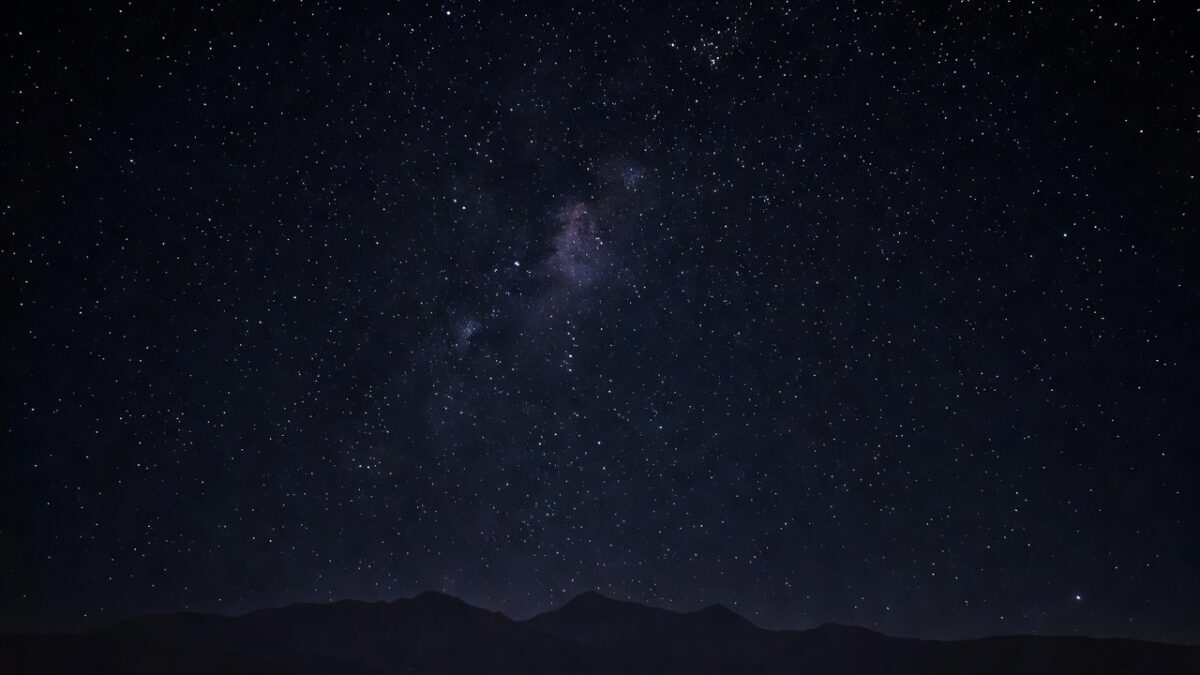Night sky filled with brightly twinkling stars above a dark mountain silhouette